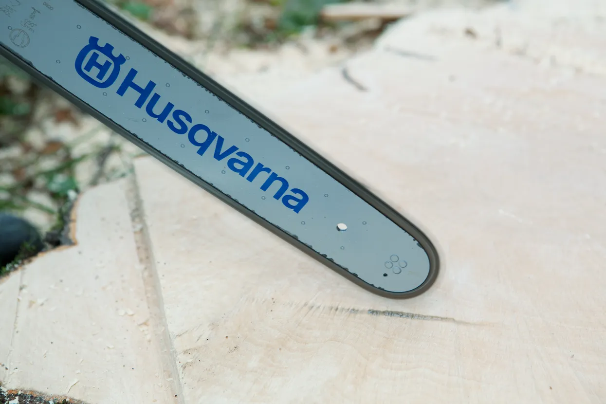 Prim-plan cu o lamă de drujbă Husqvarna sprijinită pe un butuc de copac tăiat.