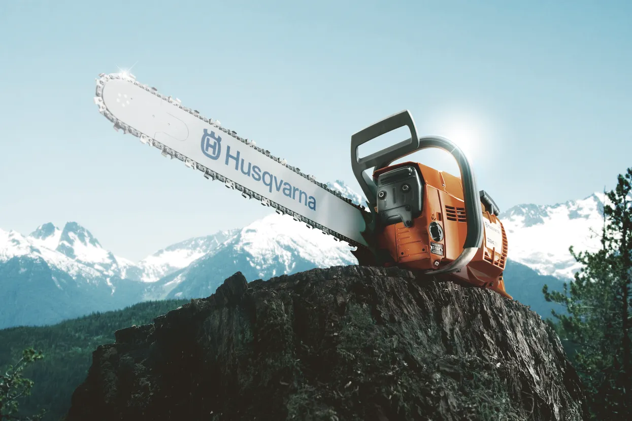 Ferăstrău cu lanț Husqvarna sprijinit pe o stâncă cu munți în fundal.