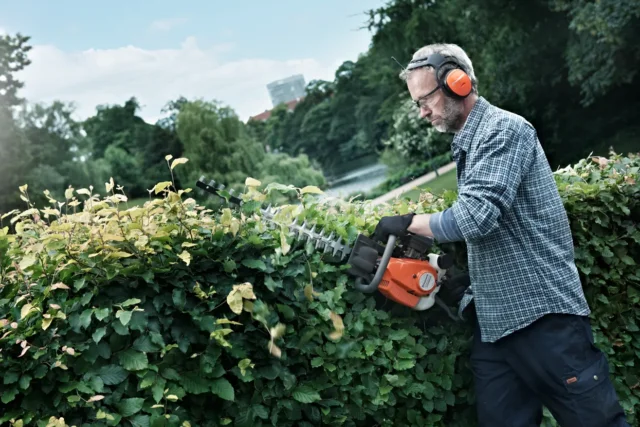 O persoană care tunde un gard viu cu un trimmer electric într-un parc.