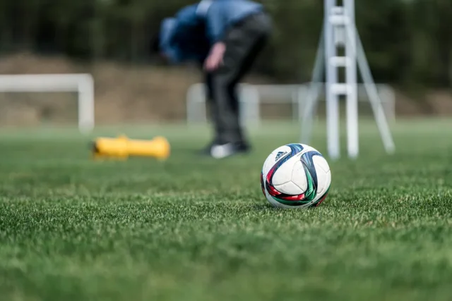 O minge de fotbal pe un teren cu iarbă cu o persoană aplecată în fundal.