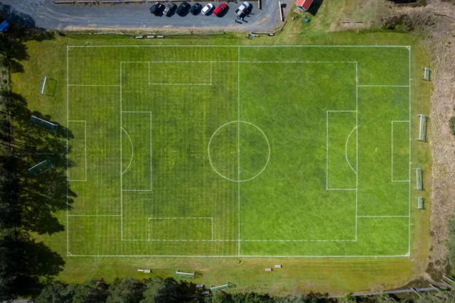 Vedere aeriană a unui teren de fotbal cu stâlpi de poartă vizibili și zonă de parcare.