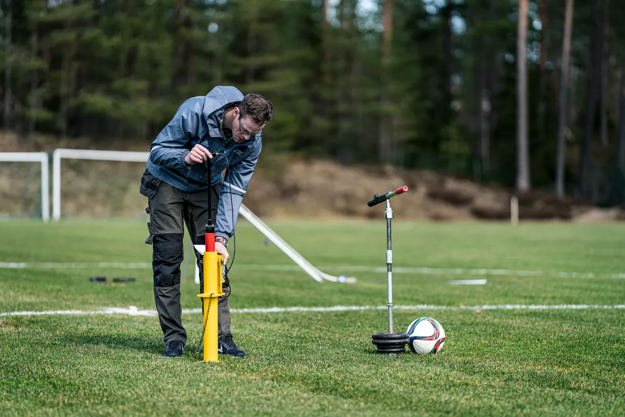 O persoană care ajustează un marcator galben de linie de teren de sport pe un teren cu iarbă, cu o minge de fotbal în apropiere.