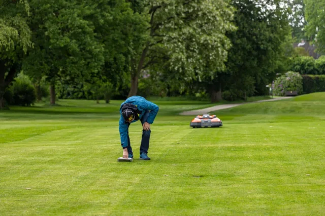 O persoană care reglează setările pe o mașină de tuns iarba robotizată într-un parc.